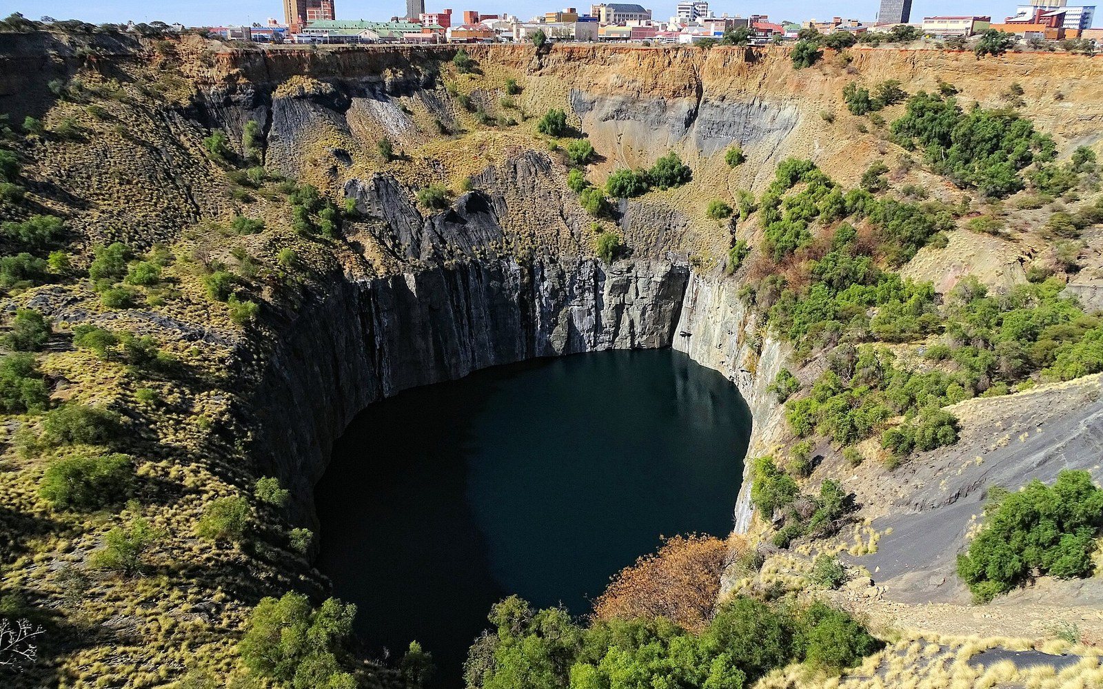 The Big Hole at Kimberley seen from the viewing platform rim, a single adult visitor standing at the rail showing the pit's scale