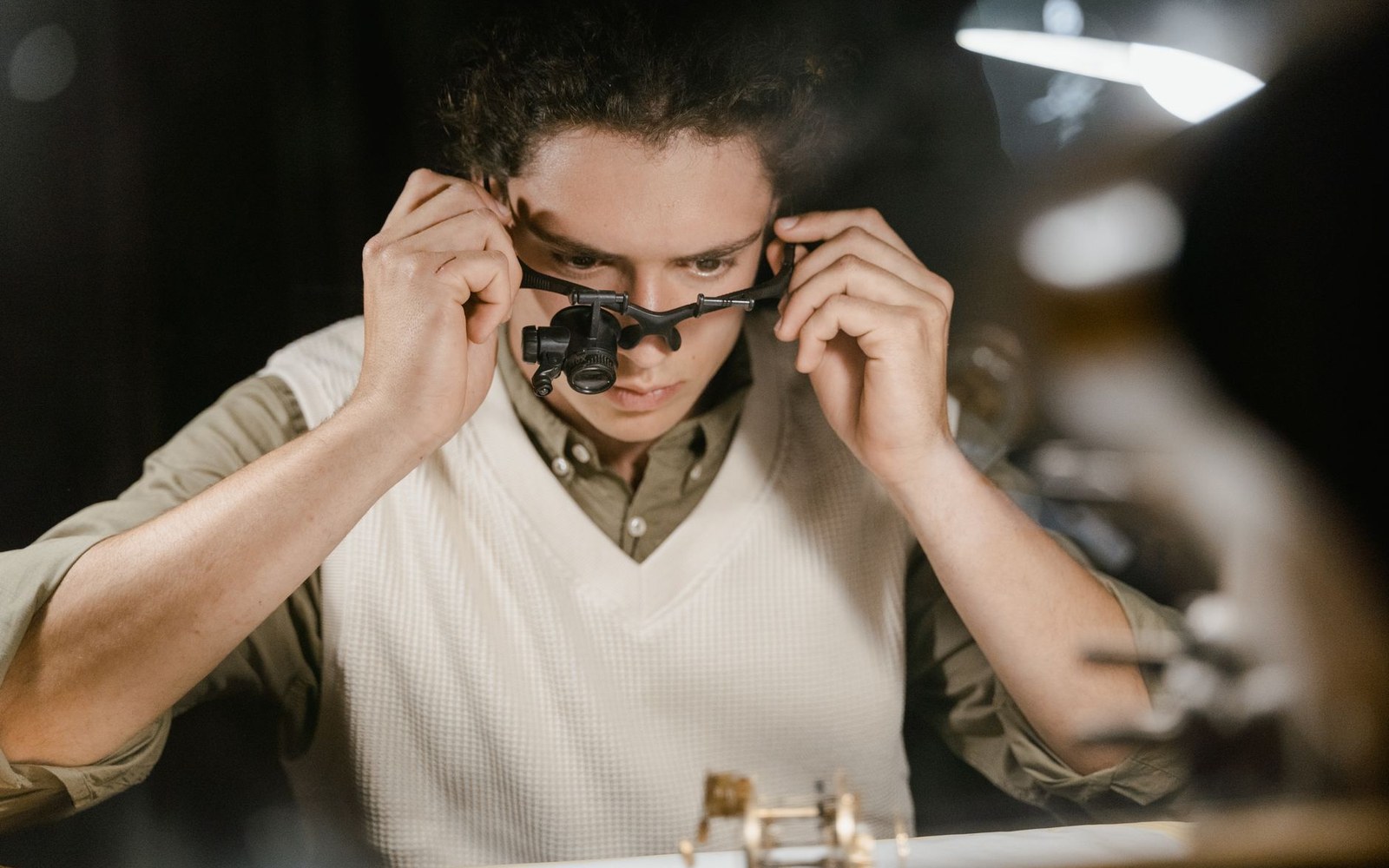 An adult gemmologist holding a cut emerald under a loupe, jardin inclusions visible, hands and magnifier filling the frame