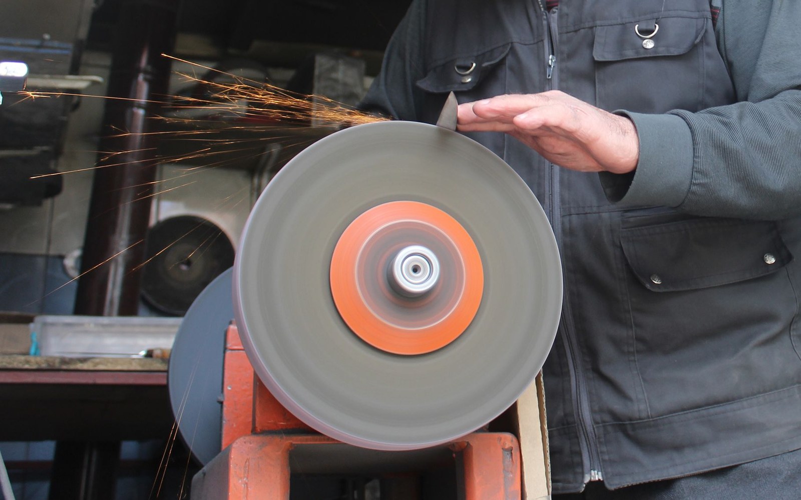 Sparks fly as a worker sharpens a blade against a spinning grinding wheel