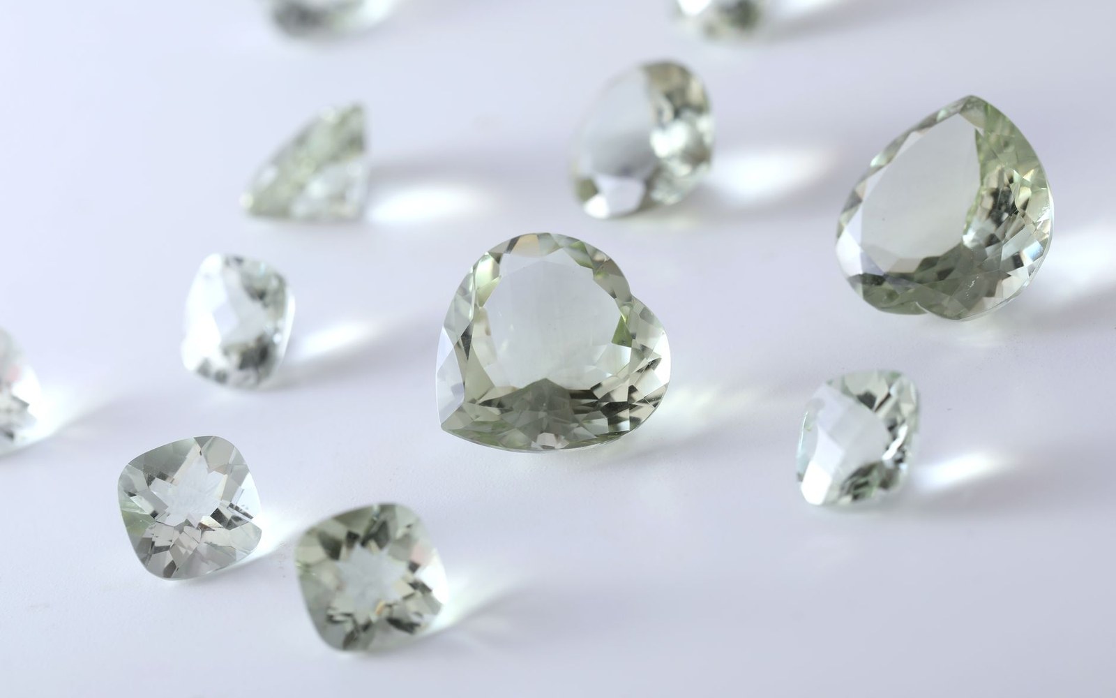 Faceted pale green gemstones in heart, cushion and pear cuts scattered on a white surface
