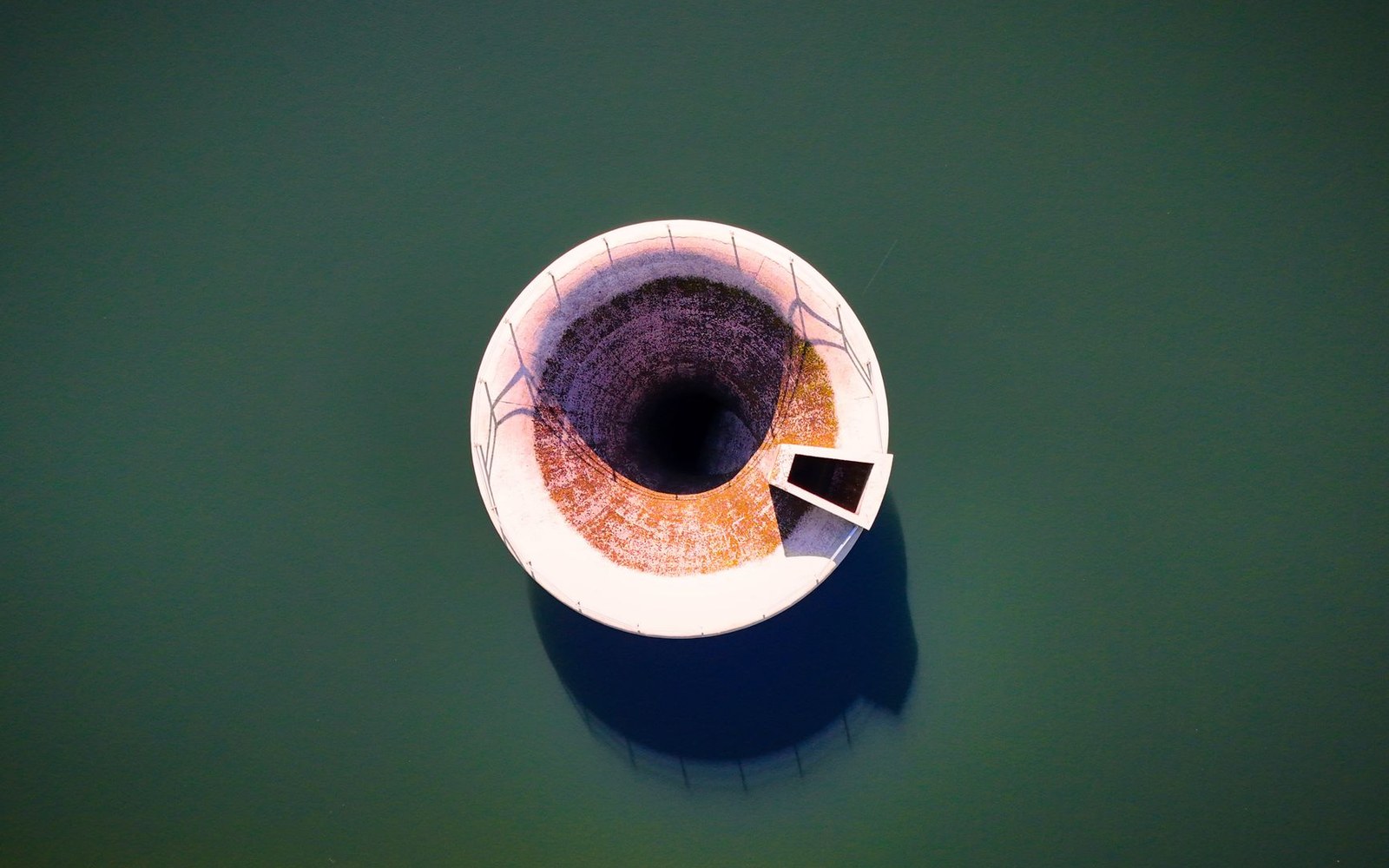 Aerial view of a circular reservoir spillway resembling a giant eye surrounded by dark water