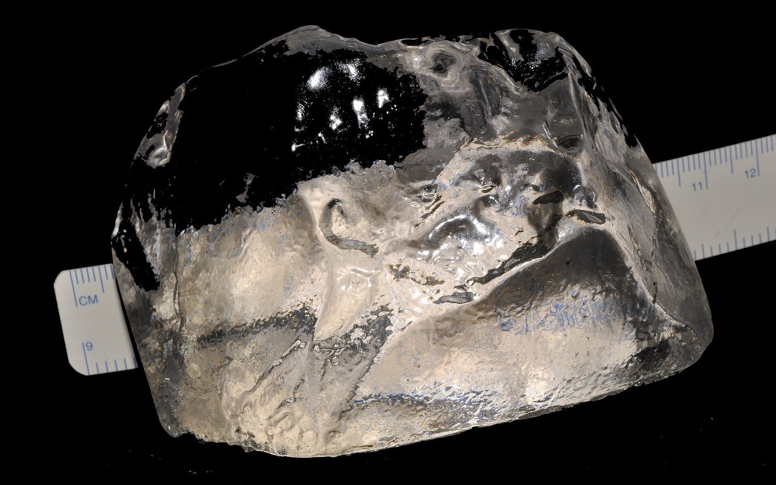 A large rough diamond crystal resting on a centimeter ruler against a black background