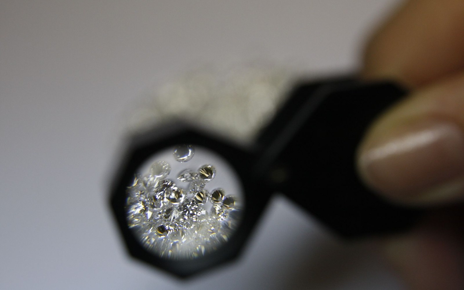 A hand holds a jeweler's loupe magnifying a cluster of loose diamonds