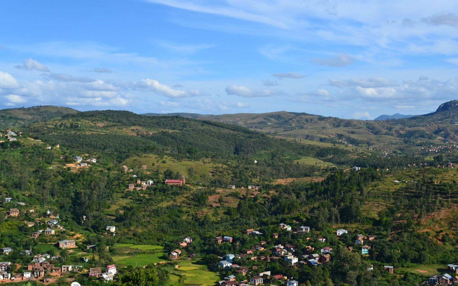 Rolling hills dotted with scattered houses and green terraced fields under a partly cloudy sky