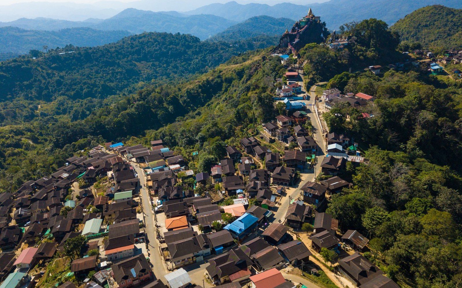 Aerial view of a hillside village with clustered rooftops leading up to a hilltop temple