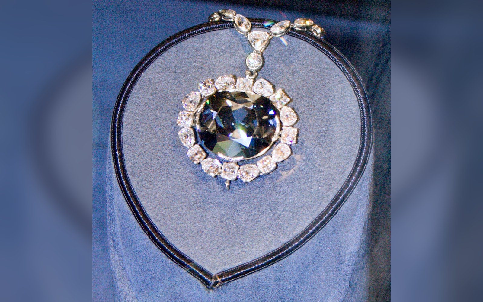 The Hope Diamond on its Winston necklace mount inside the Harry Winston Gallery vitrine, visitors' faces reflected in the glass